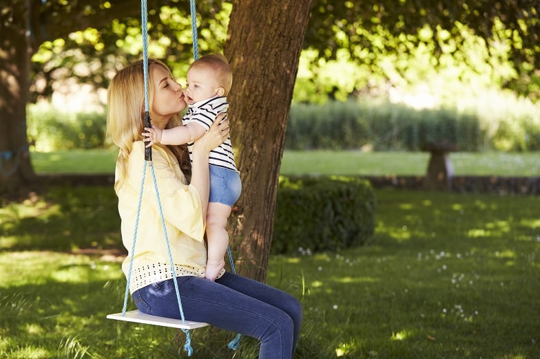 mother-kissing-baby-son-as-they-sit-on-garden-P3UPAX4-min